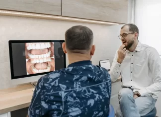 Jak świadomie zaplanować wydatki na leczenie stomatologiczne Dentysta omawia z pacjentem zdjęcia zębów wyświetlone na monitorze.