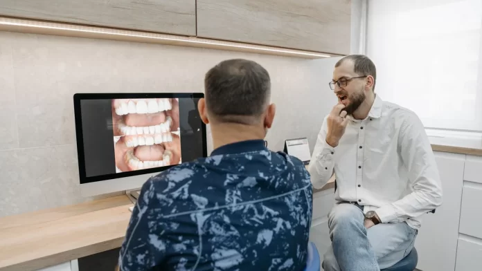 omowienie-kosztow-leczenia-stomatologicznego Dentysta omawia z pacjentem zdjęcia zębów wyświetlone na monitorze.